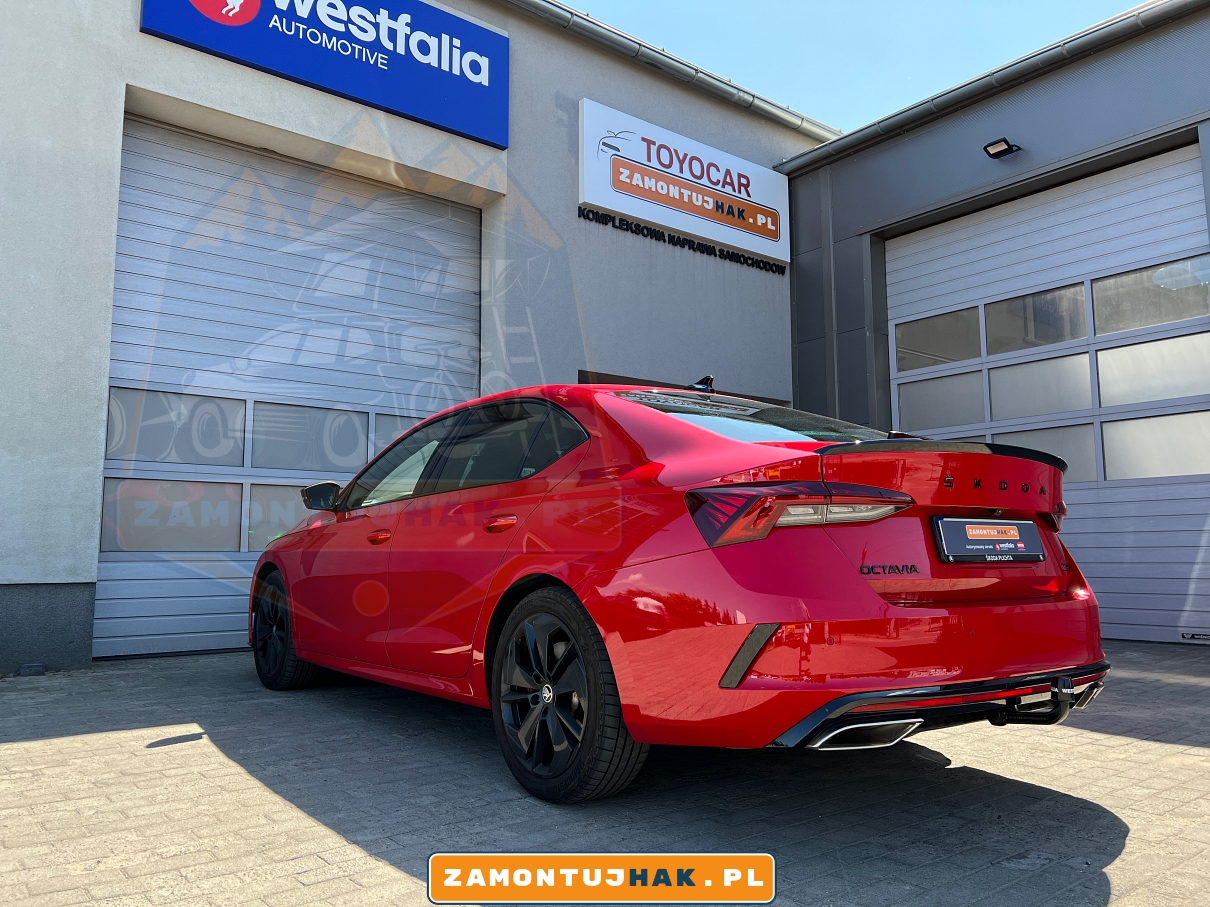 Widok z boku Skody Octavii IV RS z hakiem holowniczym, pokazujący kontrast między czerwonym lakierem a czarnym hakiem